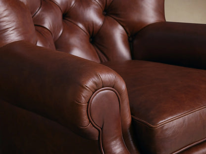 Close-up of a rich brown leather armchair, showing the rounded armrest, seat cushion, and deep button-tufted backrest.