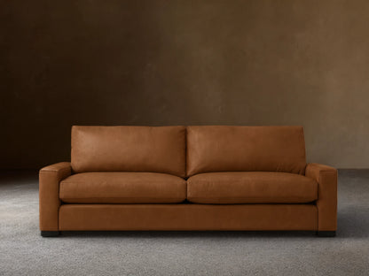 Remington Leather Sofa, medium brown, with two back and two seat cushions, and block arms, centered on a wood floor.