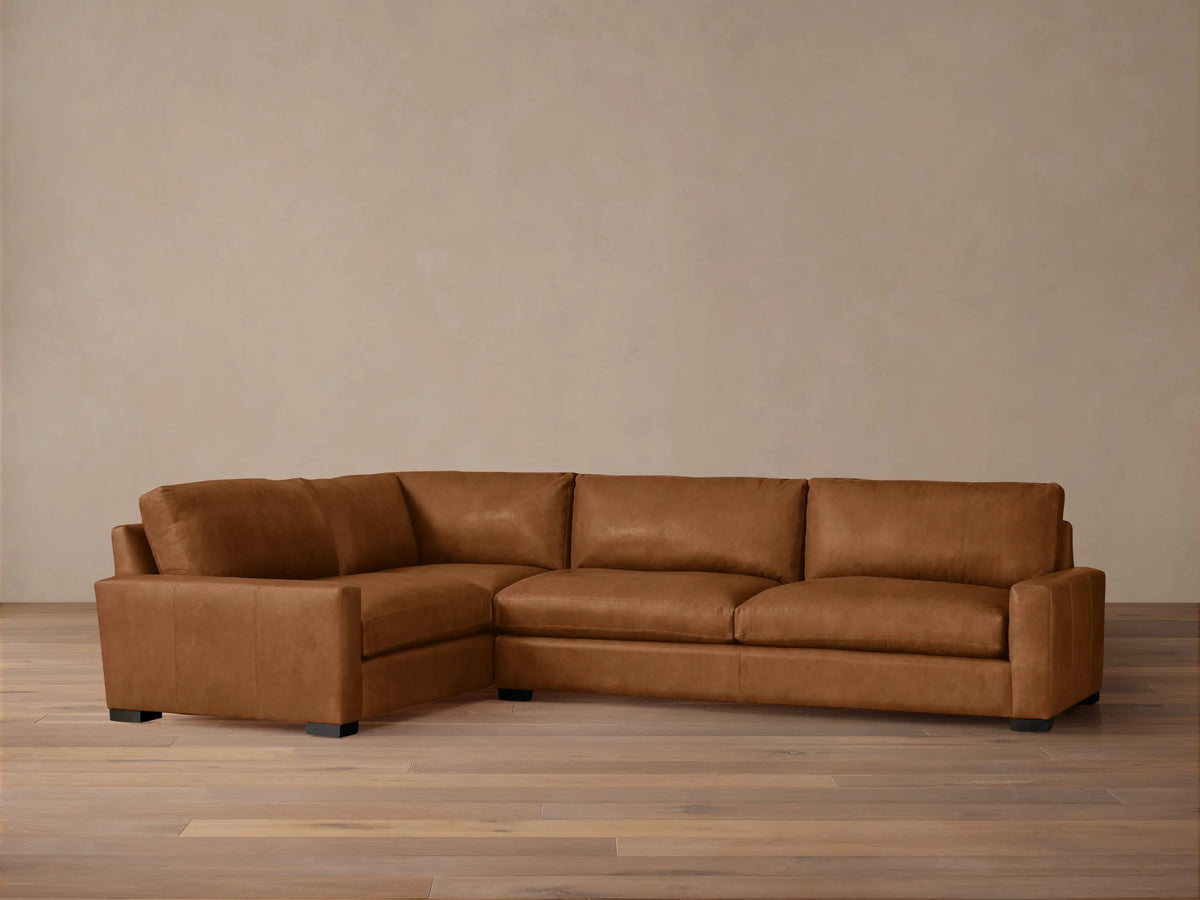 Remington Leather Two-Piece Sectional. L-shaped, warm brown leather sofa with plump cushions, dark block feet, on wood floor.