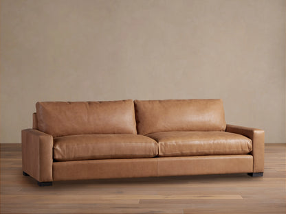 Remington Leather Sofa: A front-facing view of a warm, medium brown leather sofa with two seat cushions and squared arms on a wood floor.