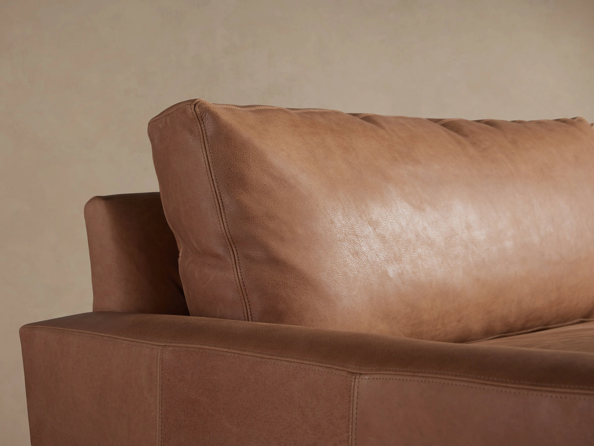 Light brown Remington Leather Sofa with two plush seat cushions and wide arms, on a wood floor against a beige wall.