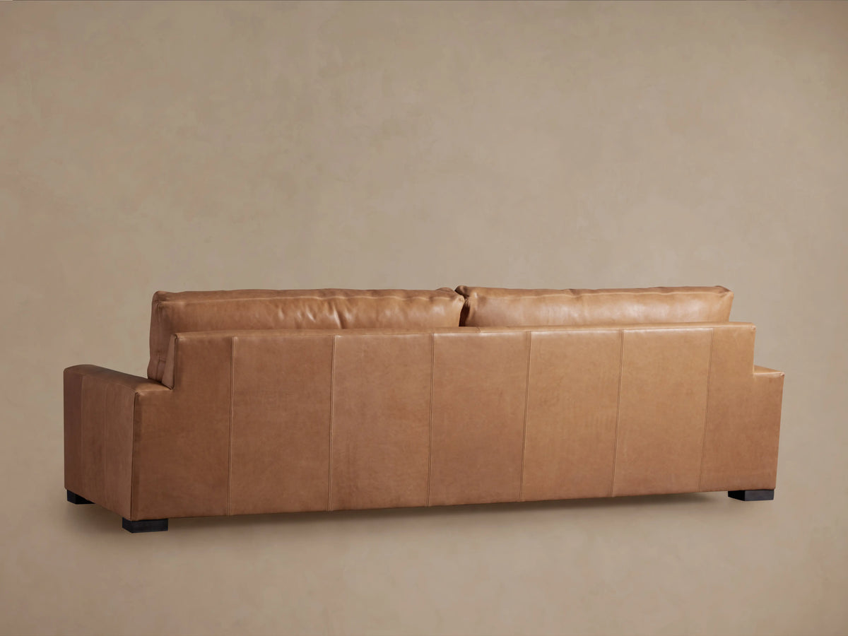 Close-up of Remington Leather Sofa; supple, warm tan leather back cushion rests against a matching armrest with visible stitching.