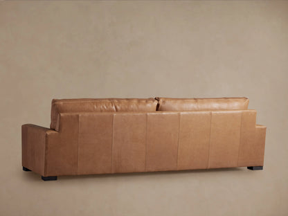 Close-up of Remington Leather Sofa; supple, warm tan leather back cushion rests against a matching armrest with visible stitching.