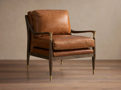 Front view of the brown leather Fisher Leather Chair. Dark wood frame with brass accents on armrests and tapered legs.