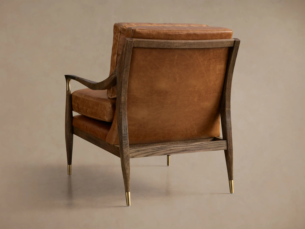 Close-up of brown leather Fisher Leather Chair, featuring dark wood frame, brass armrest accents, and visible stitching.
