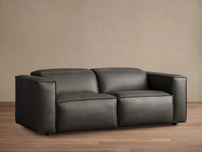 Dark gray leather Coburn Two-Piece Motion Sofa, viewed straight on. Clean lines, dark piping, on wooden floor.