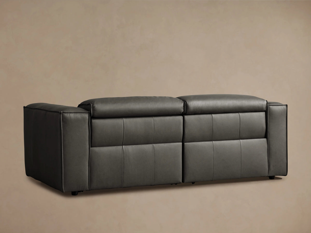 Dark gray Coburn Leather Two-Piece Motion Sofa, front view. Both recliners are upright and closed, against a light brown wall.
