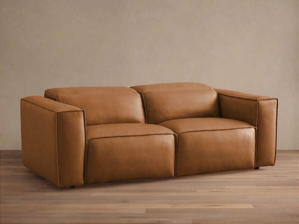 Coburn Leather Two-Piece Motion Sofa in a rich brown tone, featuring wide armrests and a minimalist design on a wooden floor.