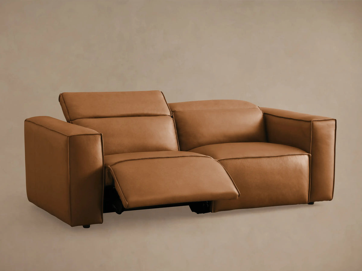 Coburn Leather Two-Piece Motion Sofa in tan leather with thick padded arms, dual backrests, and visible recline seams on beige background.