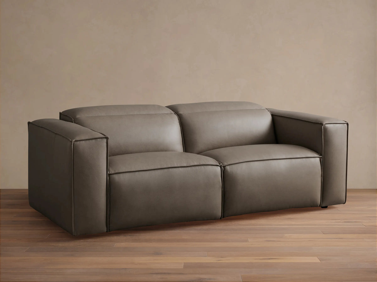 Coburn Leather Two-Piece Motion Sofa in rich brown leather with smooth, boxy arms, plush cushions, and reclining sections on a wood floor.