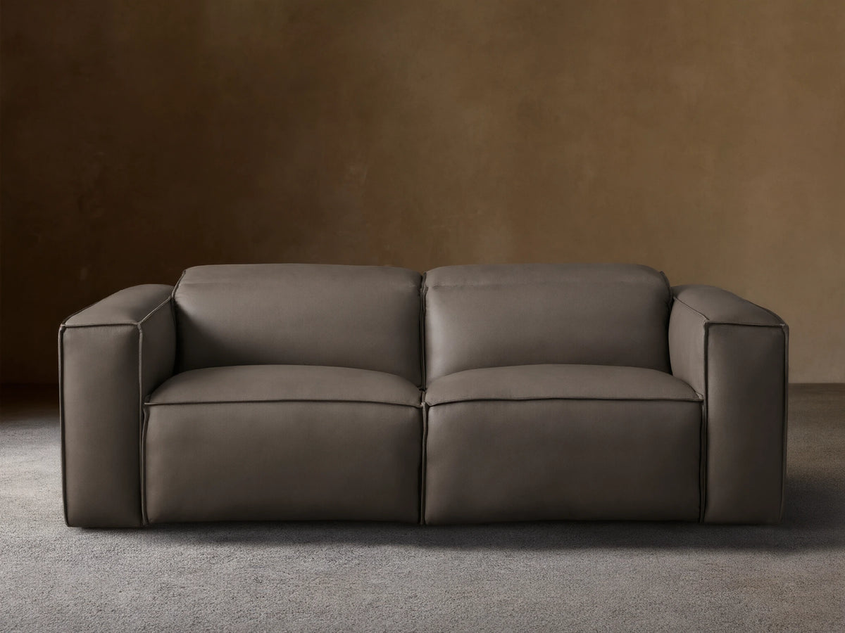 Coburn Leather Two-Piece Motion Sofa in rich brown leather with smooth, boxy arms, plush cushions, and reclining sections on a wood floor.