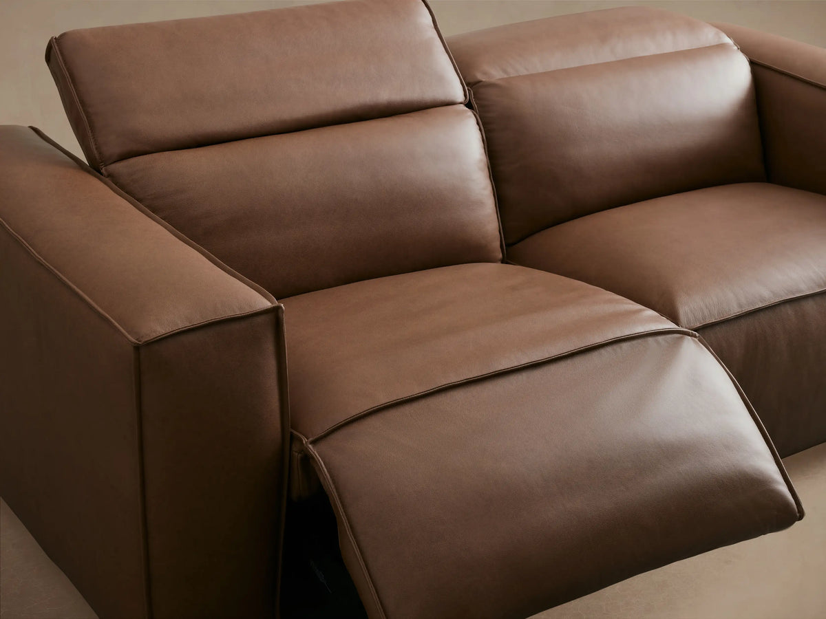 Coburn Leather Two-Piece Motion Sofa in brown leather, two reclining seats with wide arms, set on wooden floor against beige wall.