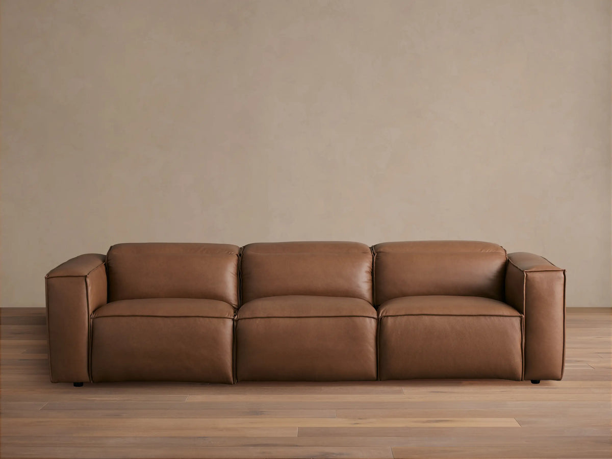 Coburn Leather Three-Piece Motion Sofa in brown leather finish, featuring three recliners with armrests on ends, positioned in a bright room.