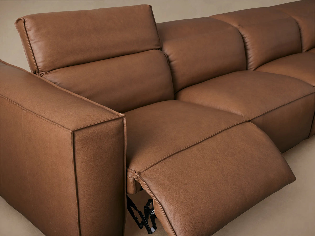 Alt text: Brown leather Coburn sectional sofa with six reclinable pieces arranged in an L-shape on a wooden floor against a beige wall.
