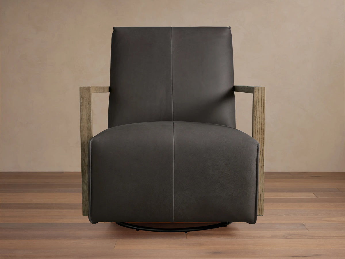 Dark brown Walsh Leather Glider with smooth leather upholstery, square wooden arms, and a black metal swivel base, on a wooden floor.
