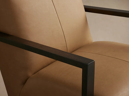 Front view of a tan leather Walsh Glider chair with dark wood-look arms, set on a light wooden floor.