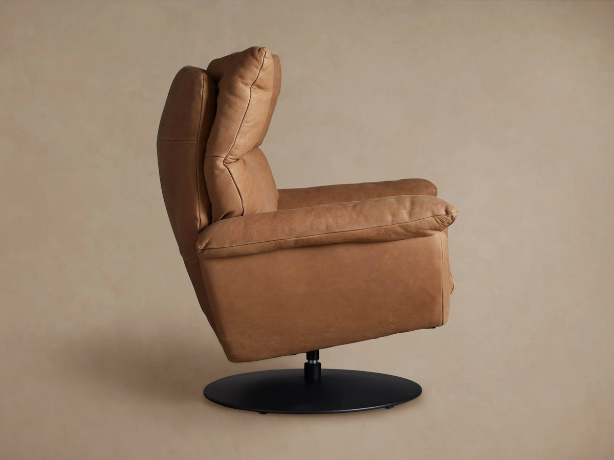 Tan leather Deacon Swivel Recliner, shown from the back-left angle, featuring a black circular swivel base and recline lever.