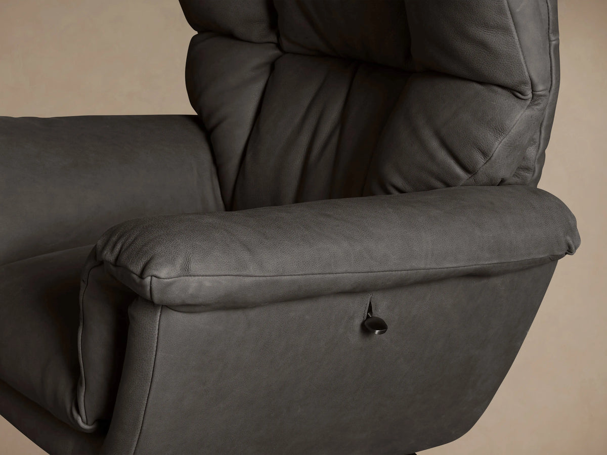 Dark grey Deacon Leather Swivel Recliner, plush & padded, with a black circular swivel base, centered against a neutral wall.