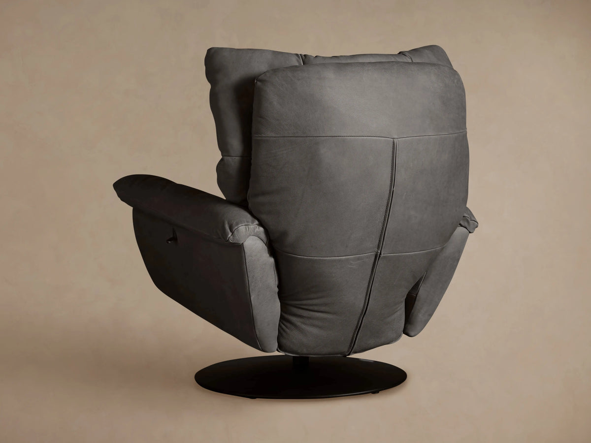 Close-up of Deacon Leather Swivel Recliner's plush dark gray leather armrest and black reclining lever on a tan background.