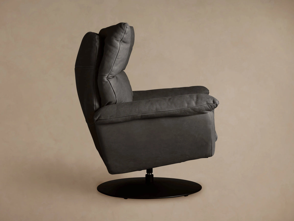Deacon Leather Swivel Recliner, charcoal gray, seen from back at an angle. Padded backrest with seams, black circular swivel base.