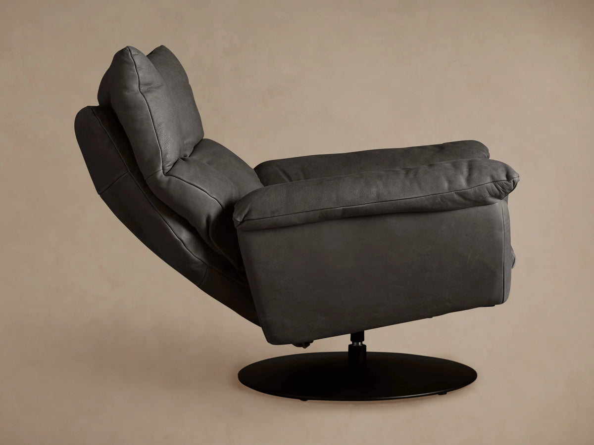 Dark gray Deacon Leather Swivel Recliner, side profile, with plush cushions and a black round swivel base against a taupe wall.