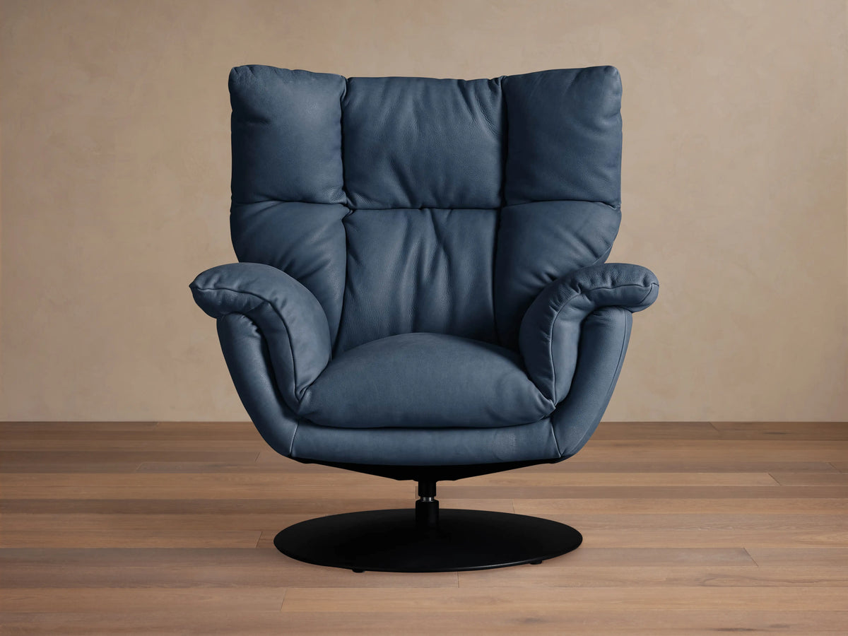 Slate blue Deacon Leather Swivel Recliner with plush cushions, black swivel base, angled front view on a wooden floor.