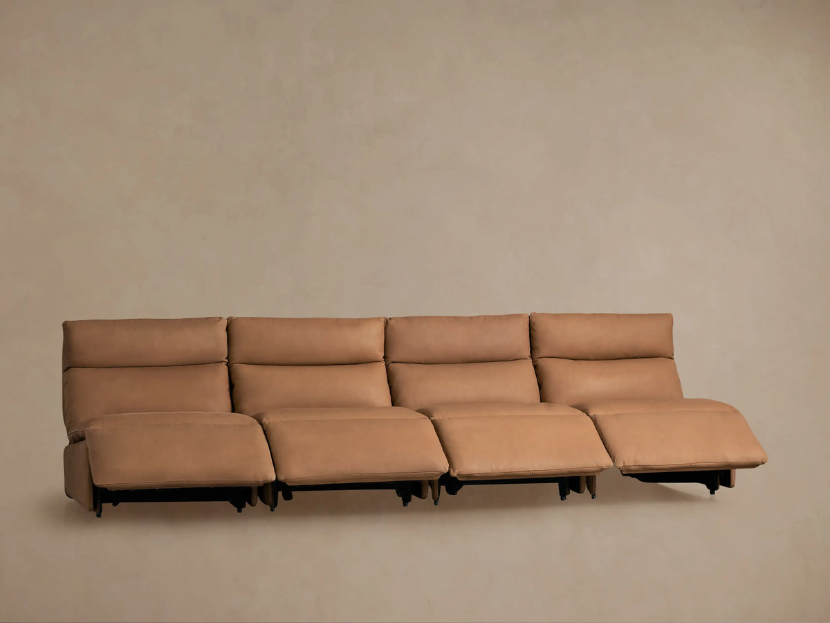Back view of Rowland Tailored Leather Four-Piece Armless Motion Modular Sofa, showing its four tan leather sections against a beige wall.