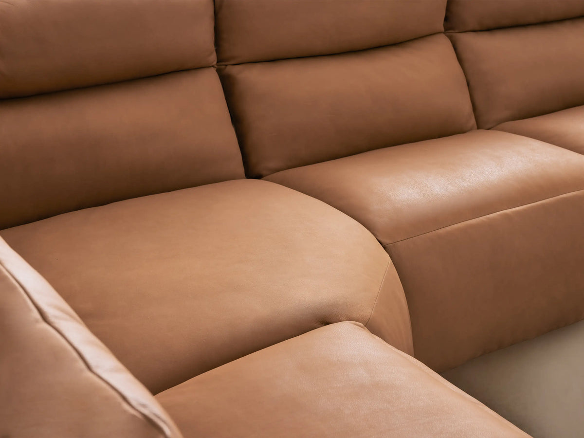 Rowland Tailored tan leather six-piece motion sectional in an L-shape on a wooden floor, against a light wall.