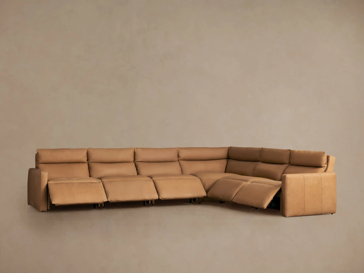Rear-side view of a light tan leather Rowland Six-Piece Motion Sectional, forming an L-shape against a neutral background.