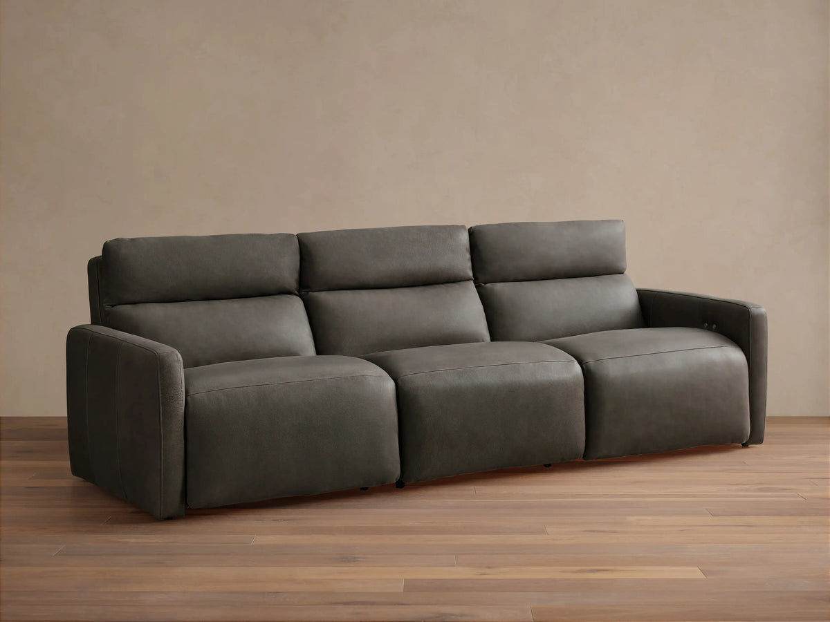 Rowland Tailored Leather Three-Piece Motion Modular Sofa, dark gray. Front-facing, on a wooden floor, against a neutral wall.