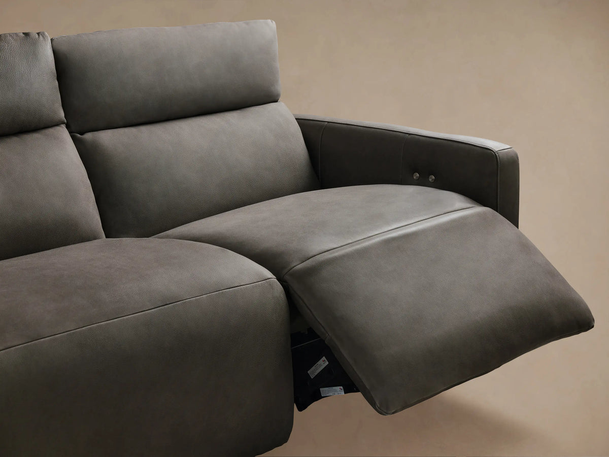Close-up of Rowland tailored leather sofa, dark gray textured backrest with vertical stitching, two silver buttons, above a lighter gray seat.
