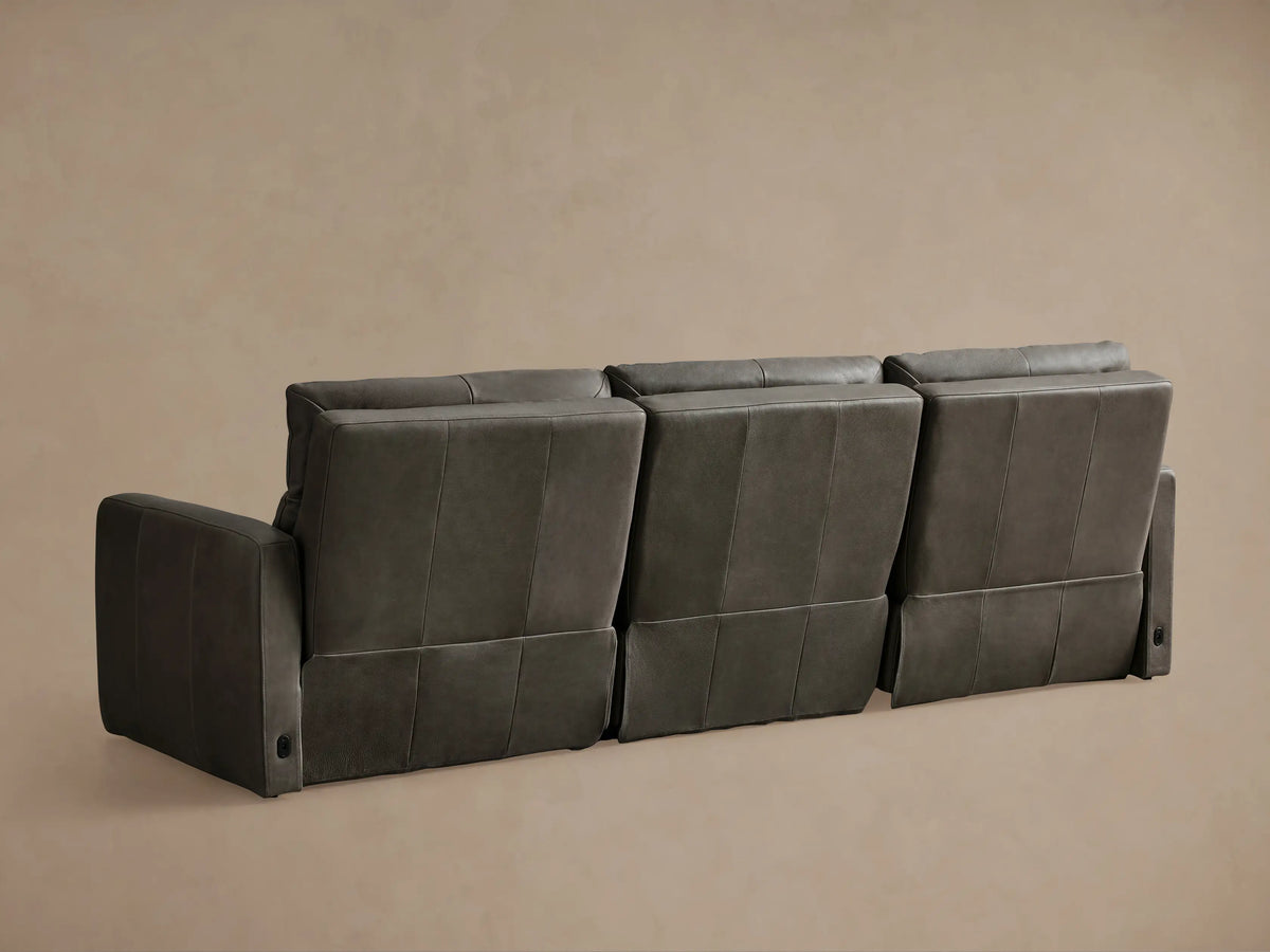 Close-up of a dark gray Rowland Tailored Leather Motion Modular Sofa with one recliner's footrest extended.