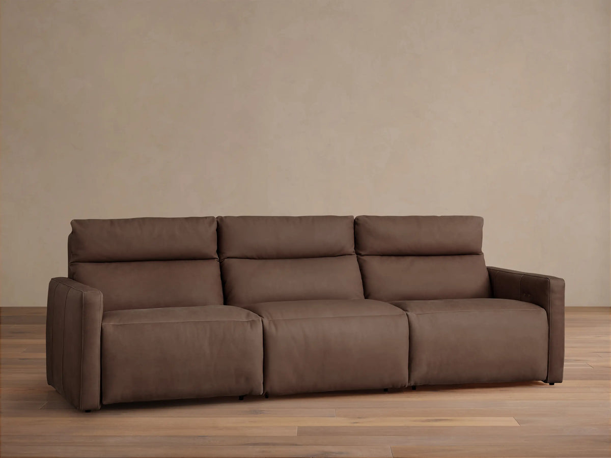 Dark brown tailored leather Rowland 3-piece motion modular sofa, front view, against a light beige wall and wood floor.