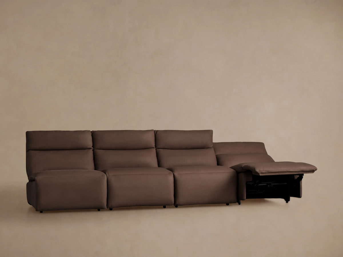 Rowland Tailored brown leather four-piece armless modular motion sofa with all footrests extended against a light brown wall.
