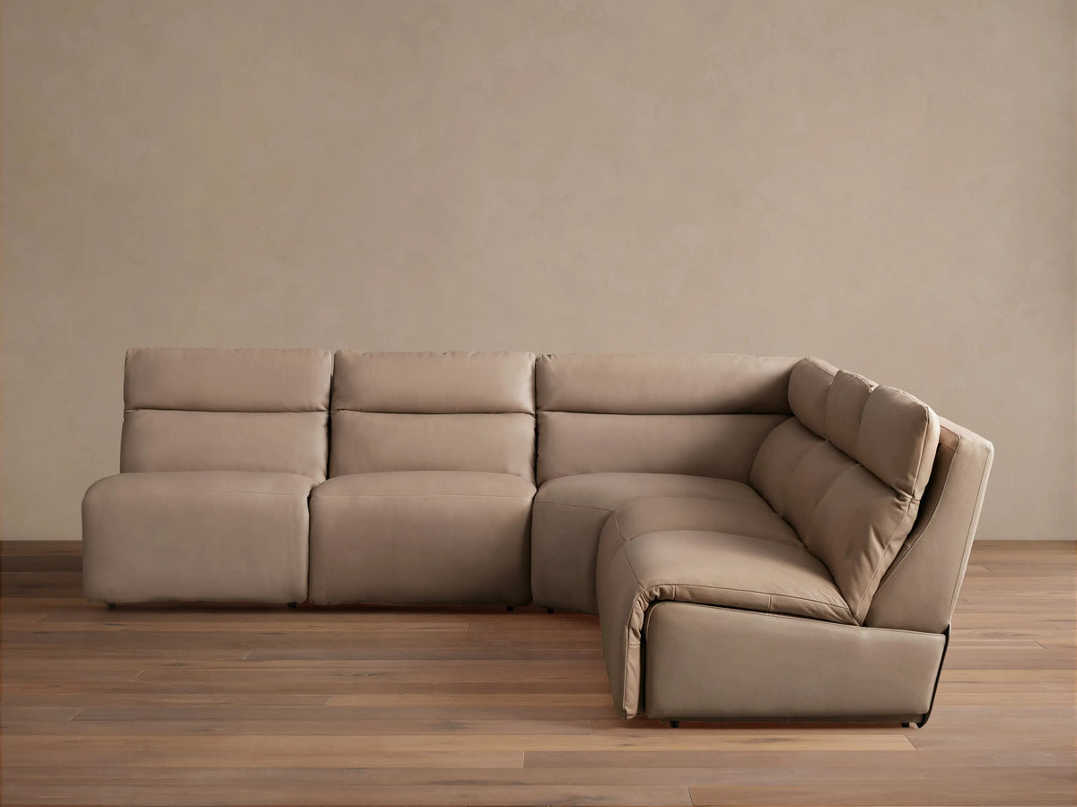 Light taupe leather Rowland 5-piece armless motion corner sectional, its corner piece partially reclined on wood floor.