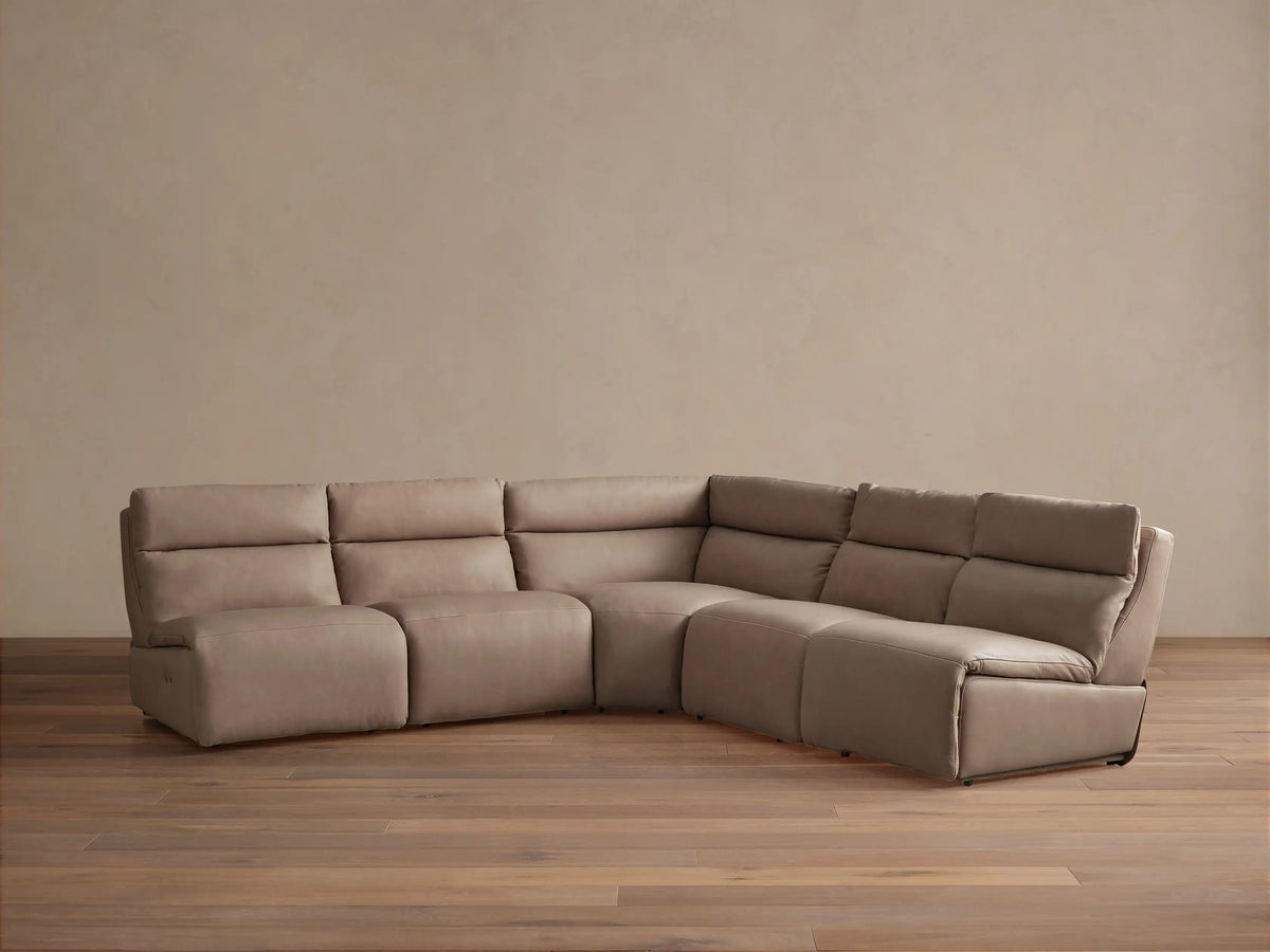 Light taupe leather Rowland 5-piece armless motion corner sectional, its corner piece partially reclined on wood floor.