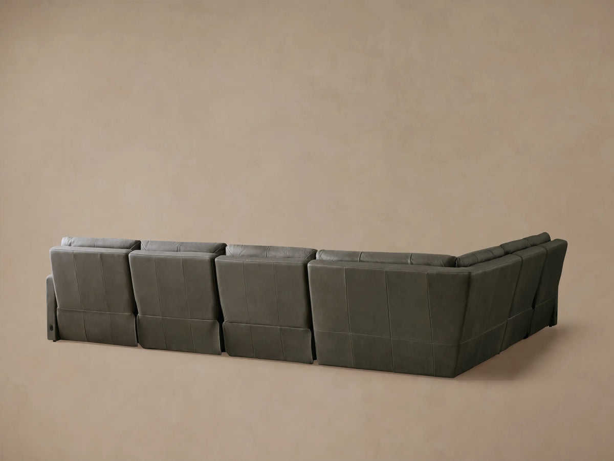 A tailored charcoal grey leather Rowland Motion Sectional, shown with a recliner's footrest extended against a beige wall.