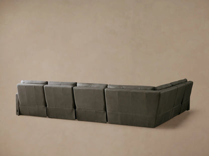 A tailored charcoal grey leather Rowland Motion Sectional, shown with a recliner's footrest extended against a beige wall.