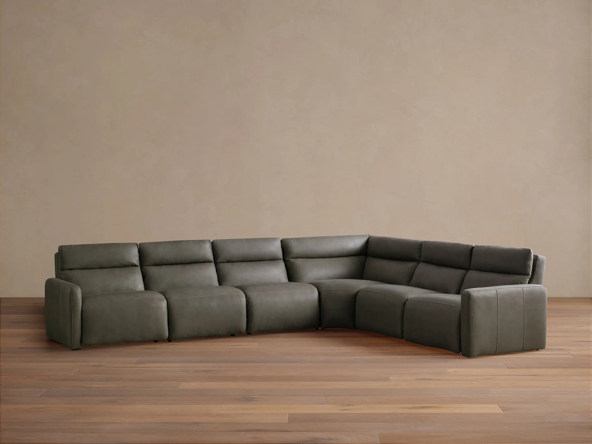 Grey-green Rowland Tailored Leather Six-Piece Motion Sectional, L-shaped, against a light wall on a wood floor.