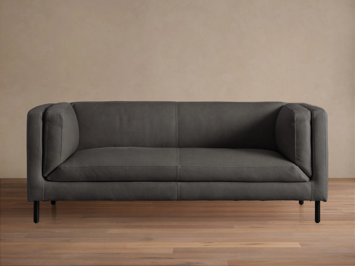 Front view of a modern dark grey Malta Leather Sofa with distinctive square arms, two seat cushions, and black recessed legs.