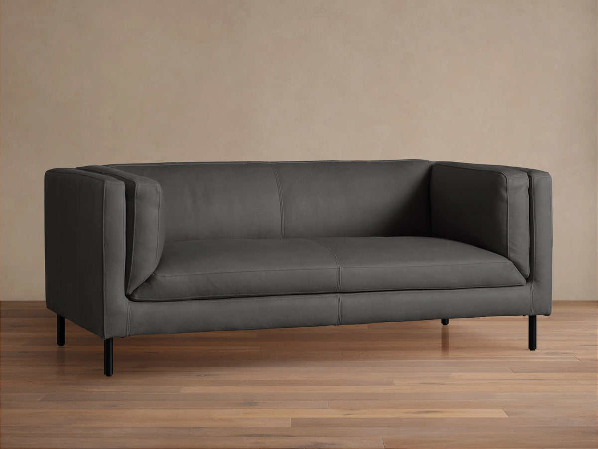 Front view of a modern dark grey Malta Leather Sofa with distinctive square arms, two seat cushions, and black recessed legs.