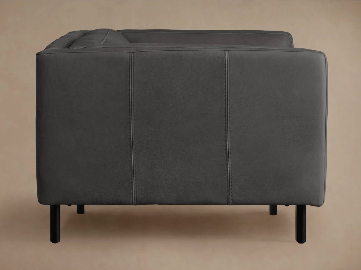 Malta Leather Sofa, dark grey, with clean square arms and black recessed legs, on a warm wooden floor, against a plain wall.