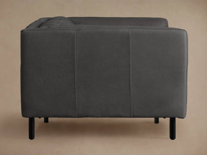 Malta Leather Sofa, dark grey, with clean square arms and black recessed legs, on a warm wooden floor, against a plain wall.