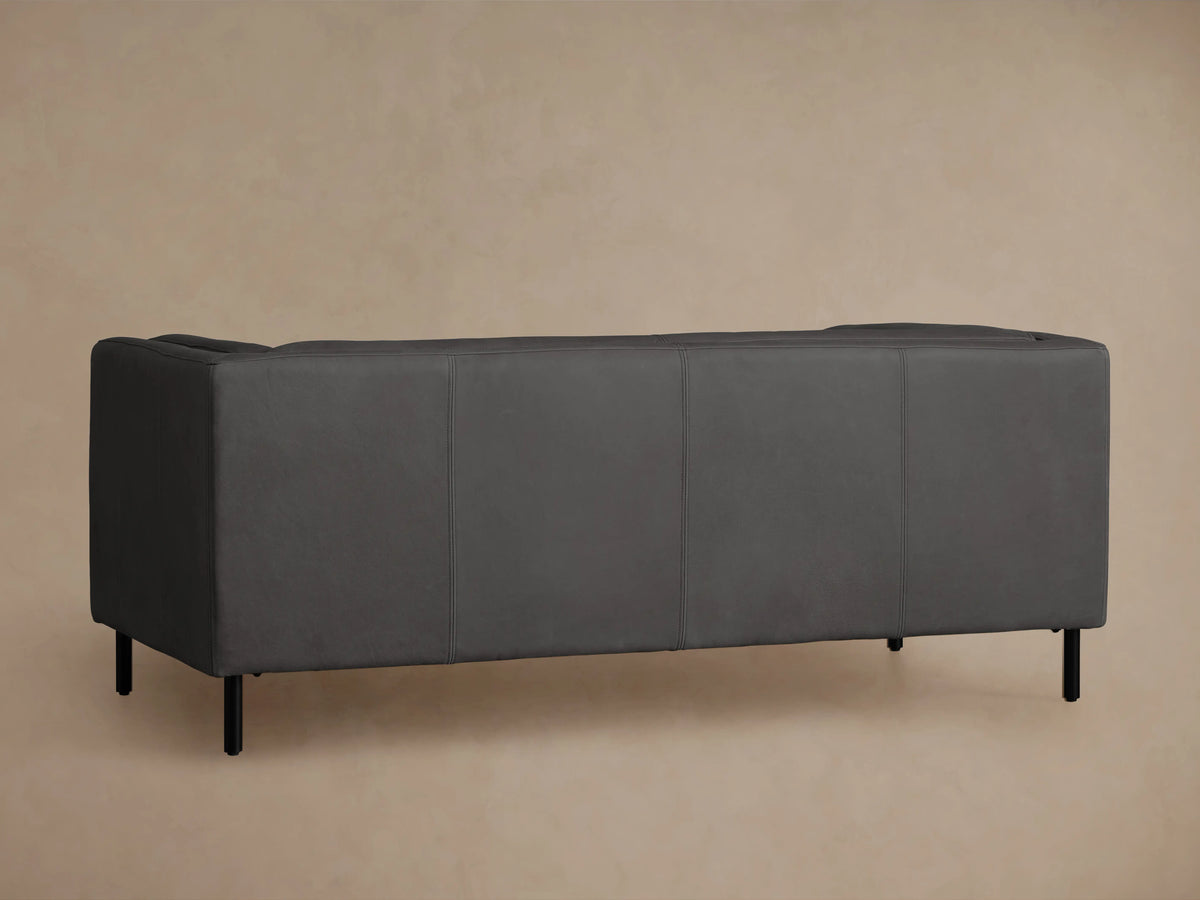Side profile of a dark gray Malta Leather Sofa, showing the armrest, side panel with vertical seams, and black metal legs.