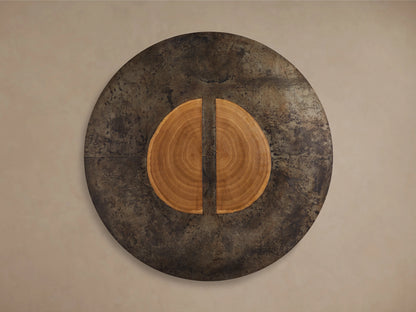 Round dining table with a unique design, featuring a dark, naturally oxidized steel surface and a central, circular wood grain pattern split by a dark line, made from reclaimed yukas trees.