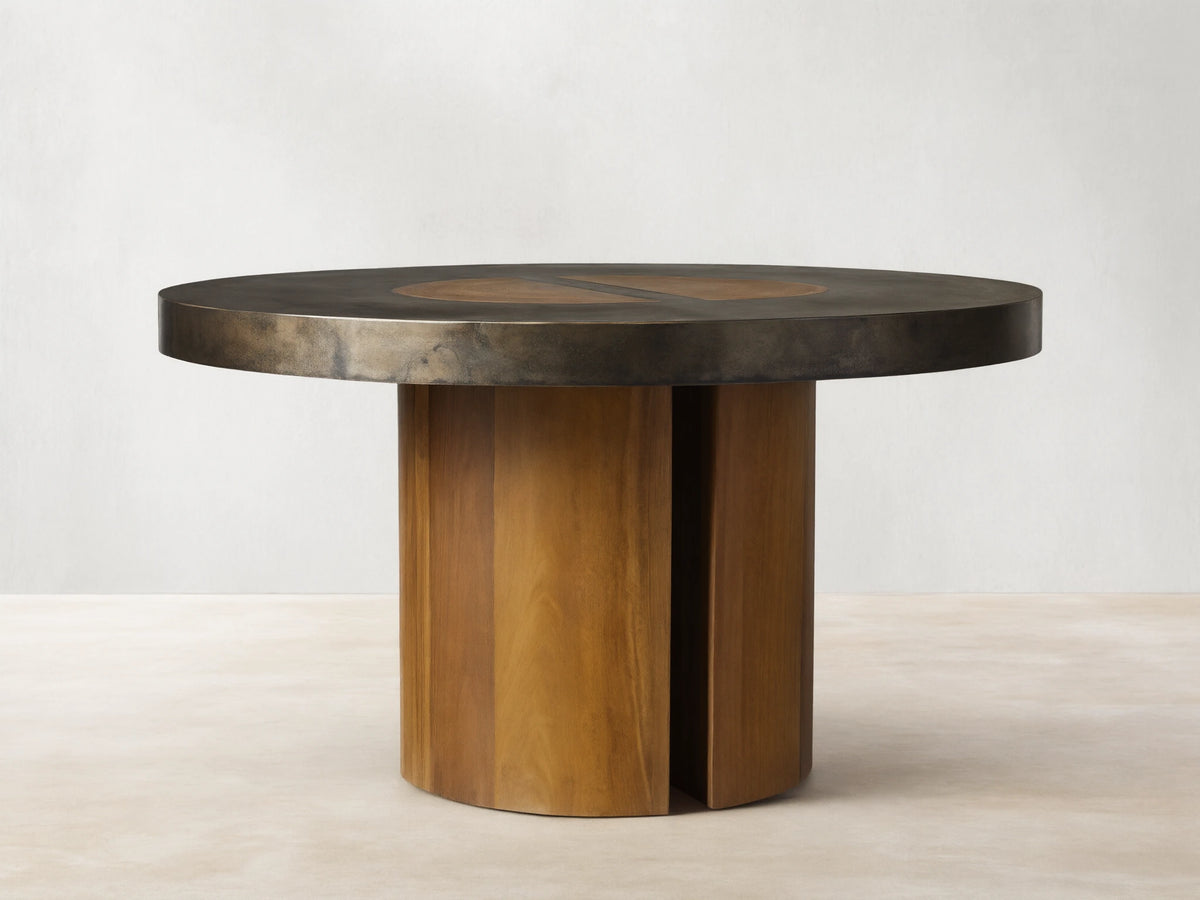Acacius Round Dining Table with a dark round top featuring oxidized steel and yukas wood, set on a sturdy wooden pedestal base.