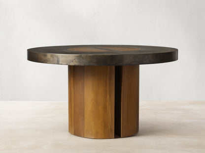 Acacius Round Dining Table with a dark round top featuring oxidized steel and yukas wood, set on a sturdy wooden pedestal base.