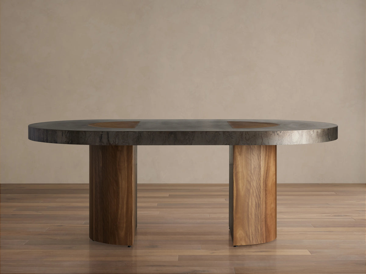 Oval Acacius Dining Table with a dark, smooth surface on two sturdy reclaimed wood legs; set in a neutral-toned room.