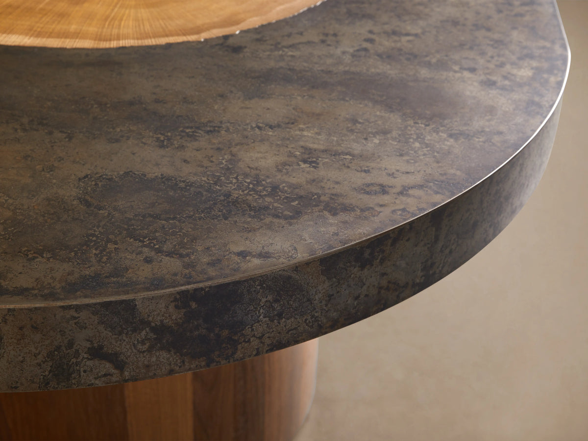 Oval Acacius Dining Table with a dark, stone-like top and distinctive wood accents on twin rectangular wooden legs, on a wood floor.
