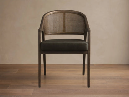 Angled rear-side view of the Aimee Faux Leather Dining Arm Chair, with a dark wood frame, woven rattan back, and dark upholstered seat.
